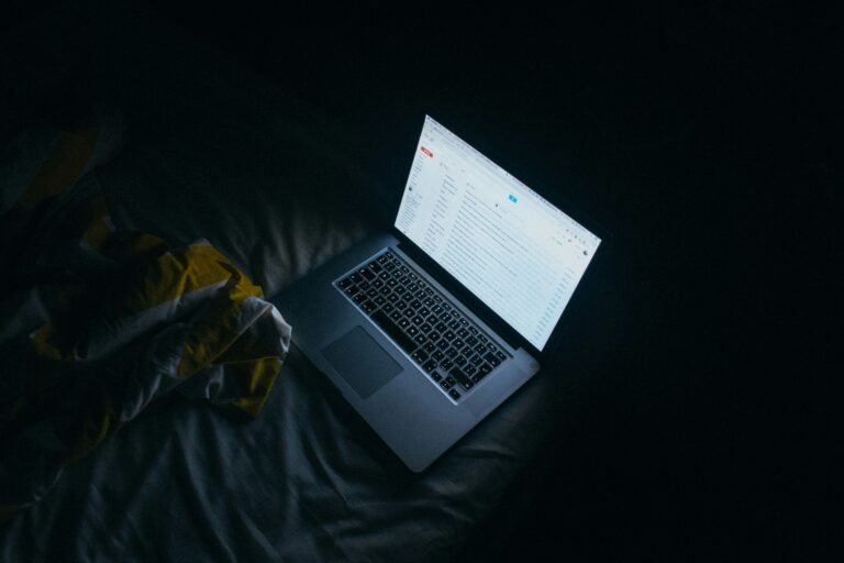 Laptop glowing on a bed in a dark room, symbolizing blurred boundaries between work and personal life