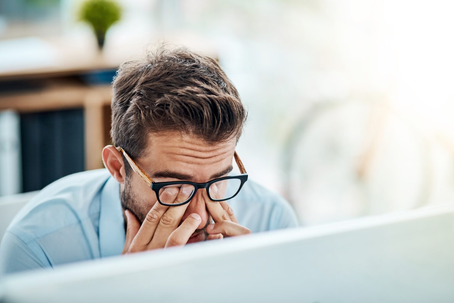 Business man showing signs of burnout with headache and stress while working at a computer in the office