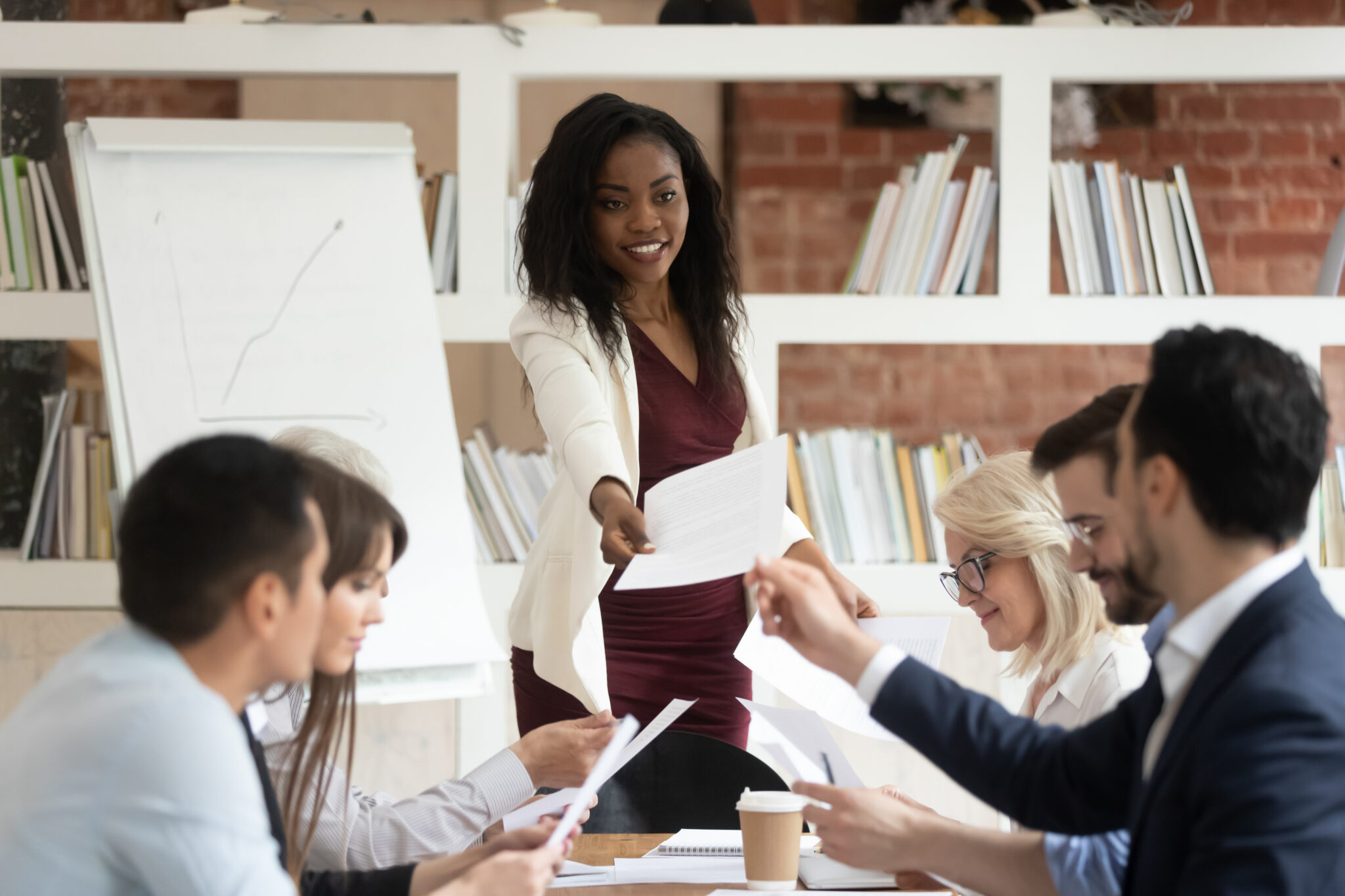 Female manager distributing tasks to a team during a corporate meeting, illustrating workload redistribution and reducing bottlenecks.