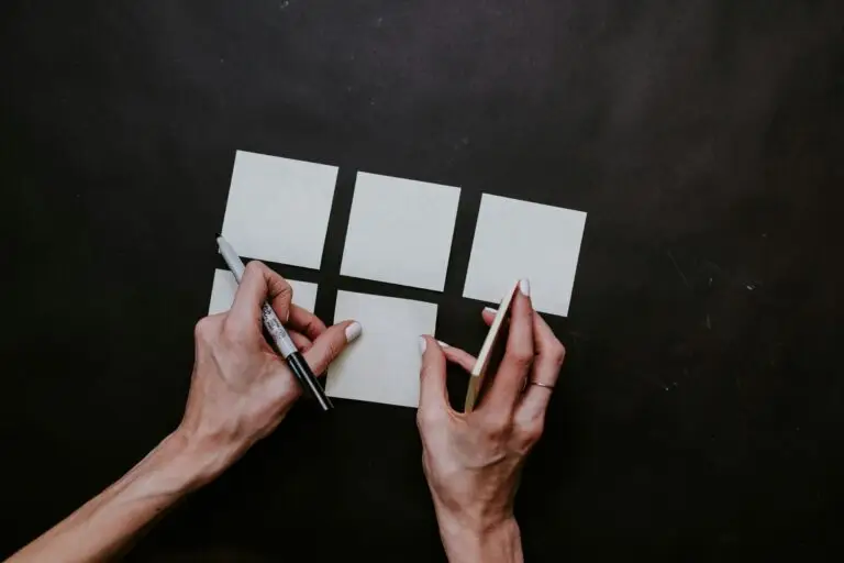 Person arranging white paper squares on a table, illustrating system design for clearer boundaries and reduced workplace pressure.