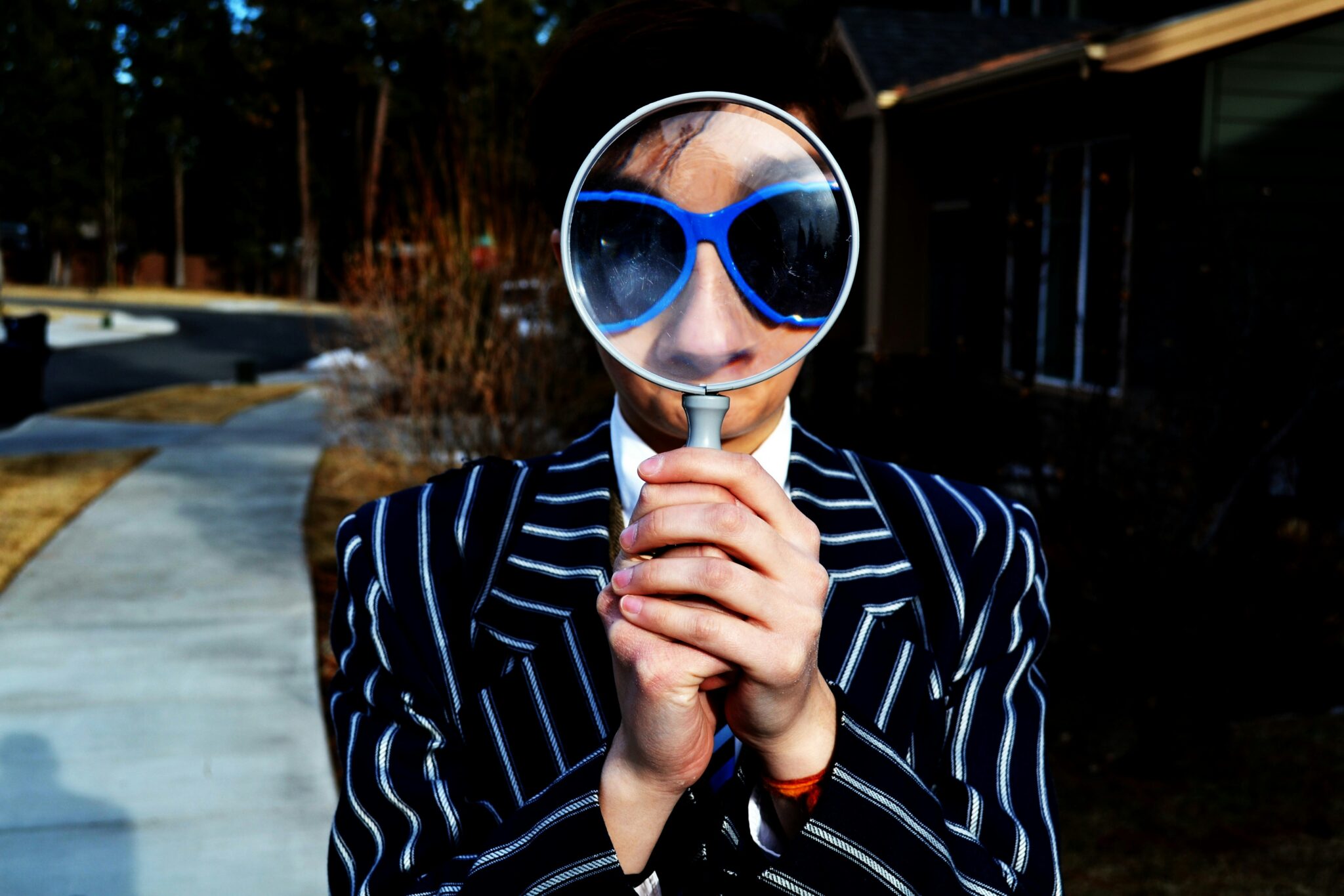 Man in a pinstripe suit holding a magnifying glass to his face, symbolising close examination of stress and underlying patterns.